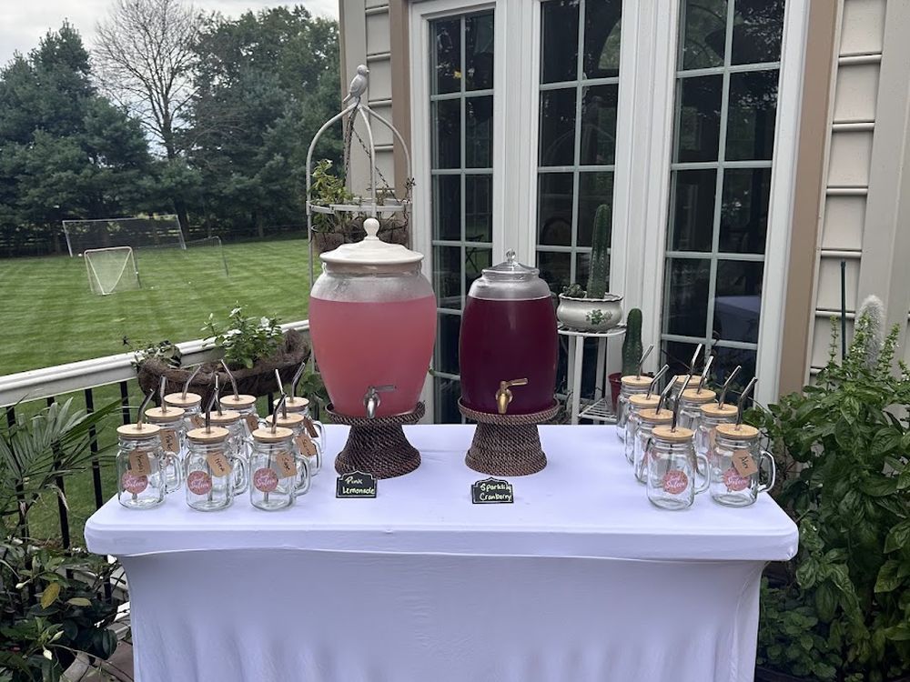 Two drink dispensers and glass jars on a table covered with a white floor length linen